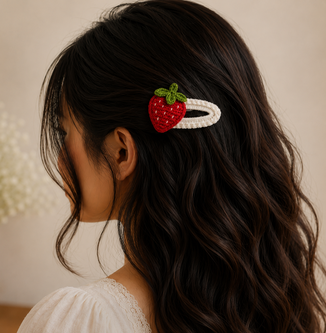 A close-up side view of a woman with long, wavy dark brown hair wearing a white braided hair clip adorned with a red strawberry embellishment and green leaves.