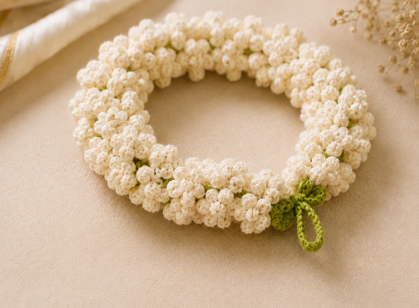 A handmade crocheted floral wreath made of small cream-colored flowers with a small green leaf accent, displayed on a neutral beige background.