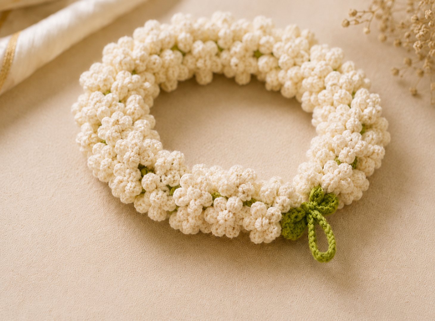A handmade crocheted floral wreath made of small cream-colored flowers with a small green leaf accent, displayed on a neutral beige background.