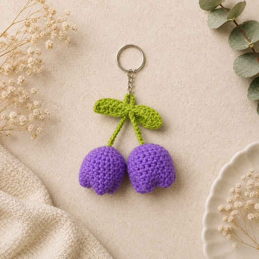A handmade crochet double tulip keychain in purple with leafy green accents — a charming, everlasting floral charm perfect for gifting or everyday carry.