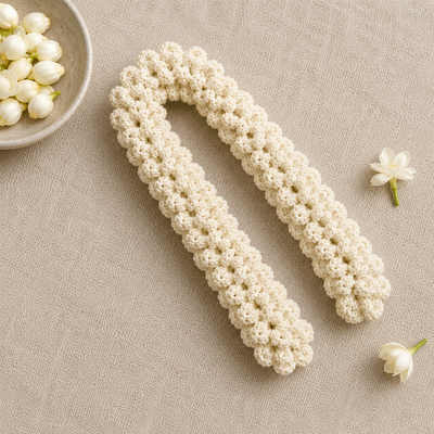 A cream-colored crocheted hair claw clip shown on a textured beige fabric background with decorative white flowers.
