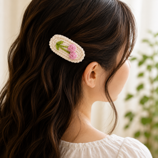 A woman shown from the back wearing a cream crocheted hair clip decorated with pink flowers and green stems, attached to her dark brown wavy hair.