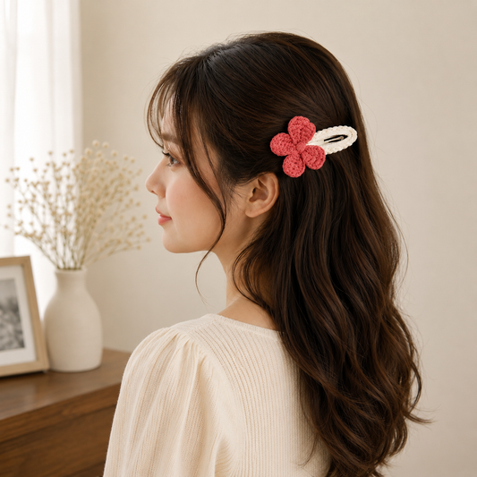 A woman in profile wearing a pink crocheted flower hair clip with a white elastic band, shown in a softly lit indoor setting.
