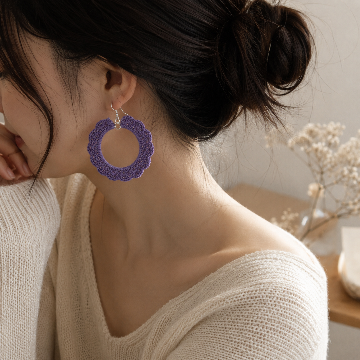 A woman wearing a textured purple circular dangle earring with a silver-toned hook, shown in a close-up profile view against a softly blurred indoor background.