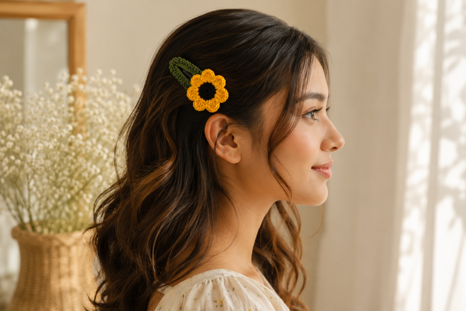 A woman in profile wearing a crocheted yellow sunflower hair clip with a green leaf accent, styled in a warm, softly lit indoor setting.