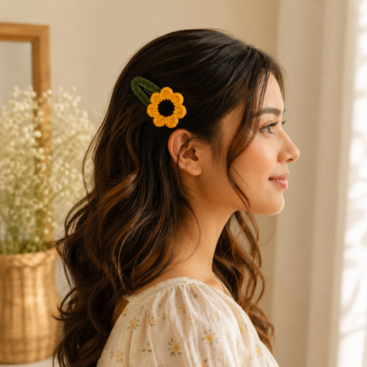 A woman in profile wearing a crocheted yellow sunflower hair clip with green leaves, styled in a warm, softly lit indoor setting.